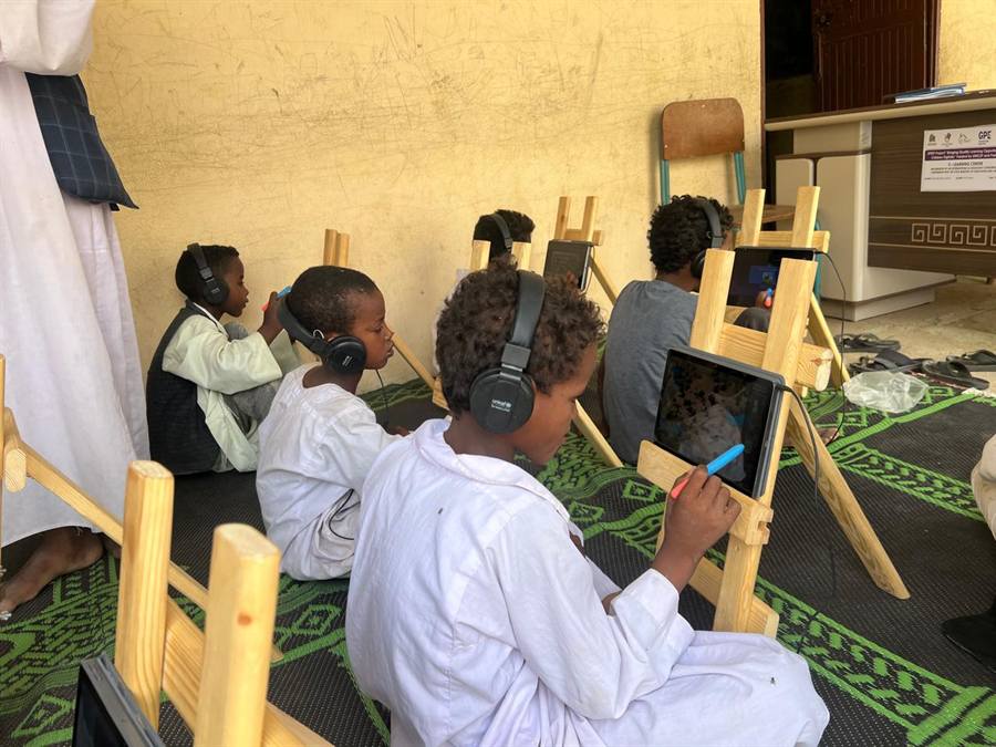 Young children sit on floor mats using tablets in an early learning classroom.